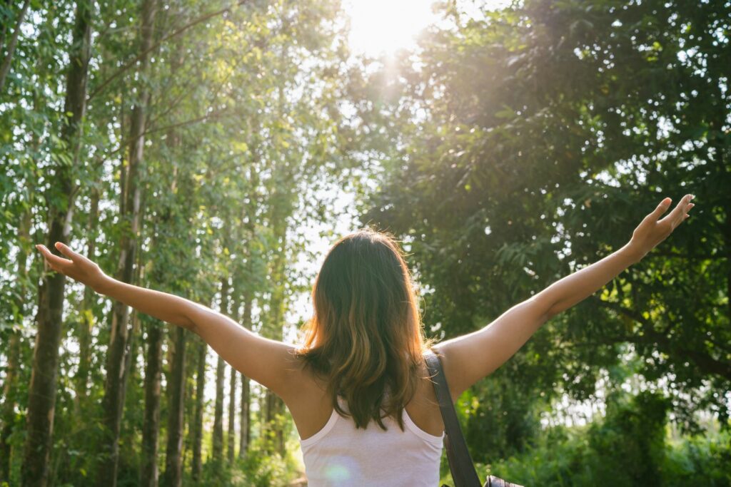 femme de dos dans la foret avec les bras en croix inspirant le bien être la liberté