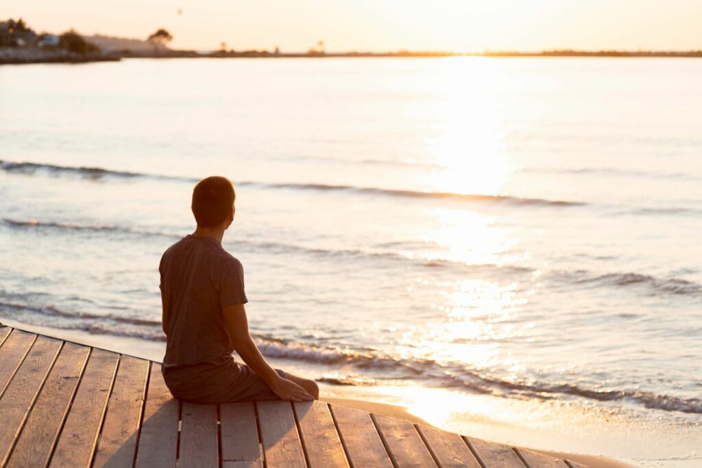 homme méditant de dos assis face au front de mer synonyme d'apaisement, de relaxation.