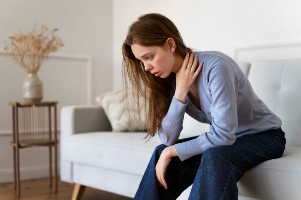 jeune femme assise sur un canapé souffrant de symptome de fibromyalgie