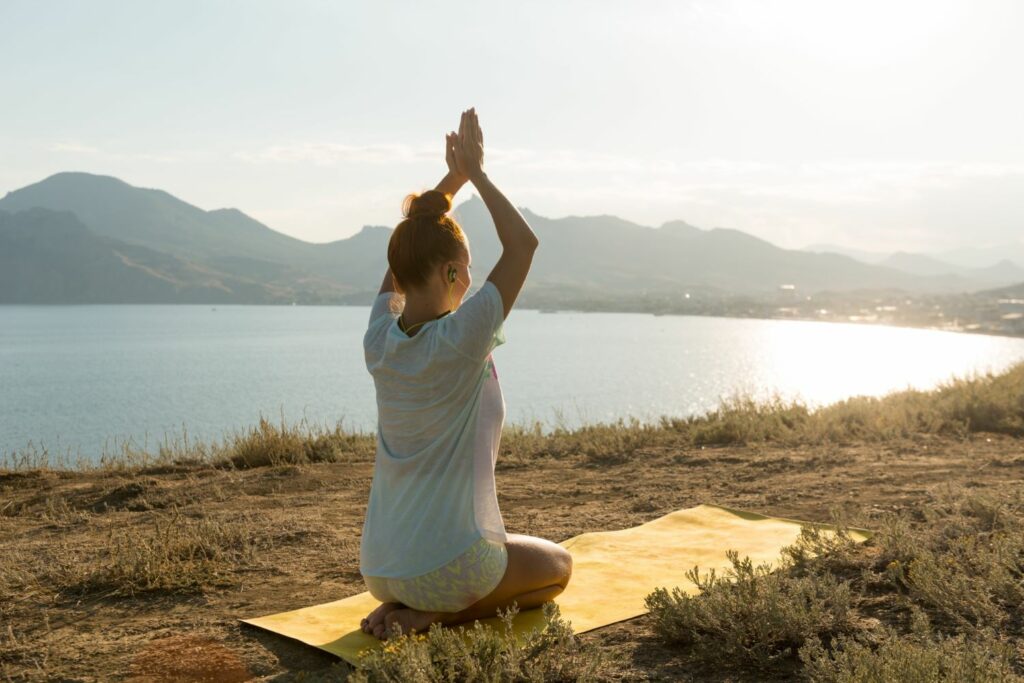 jeune femme en position yoga face au soleil sur une colline inspirant le bien être émotionnel