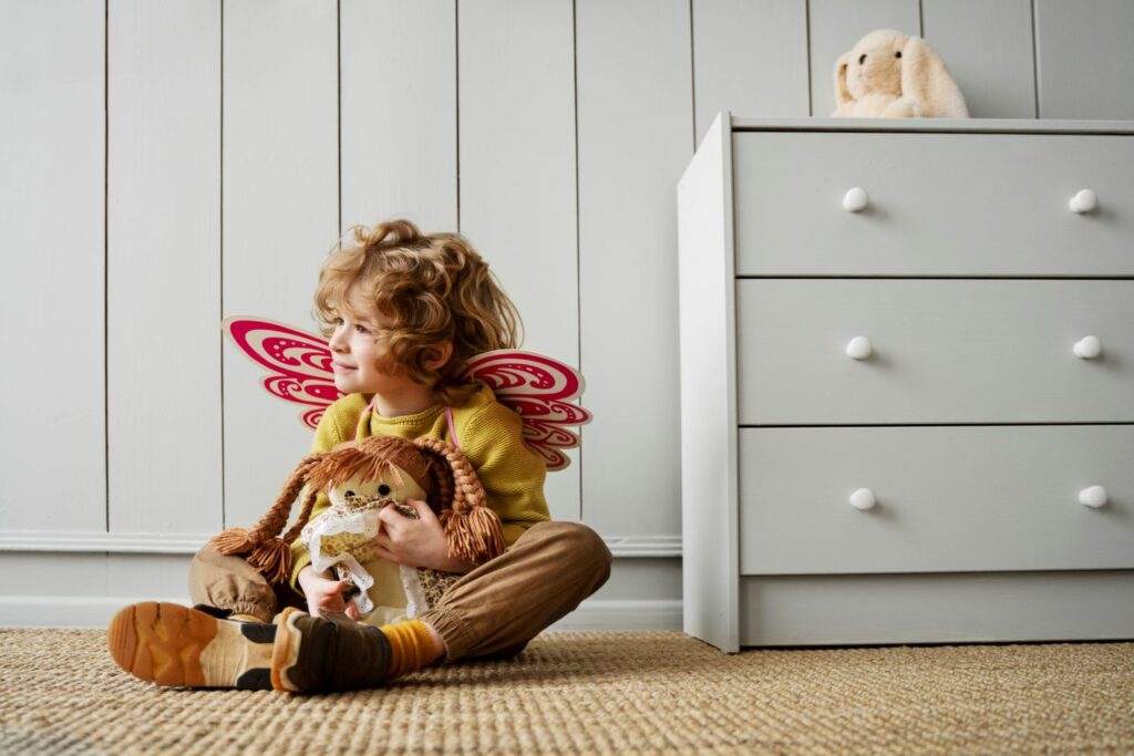 petit enfant assis sur le sol souriant avec des ailes de papillons et un nounours rappelant son enfant intérieur