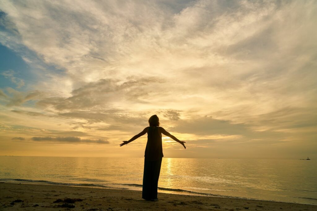 silhouette d'une femme en bord de plage levant les bras inspirant la liberte de sortir de sa peur de rejet et abandon