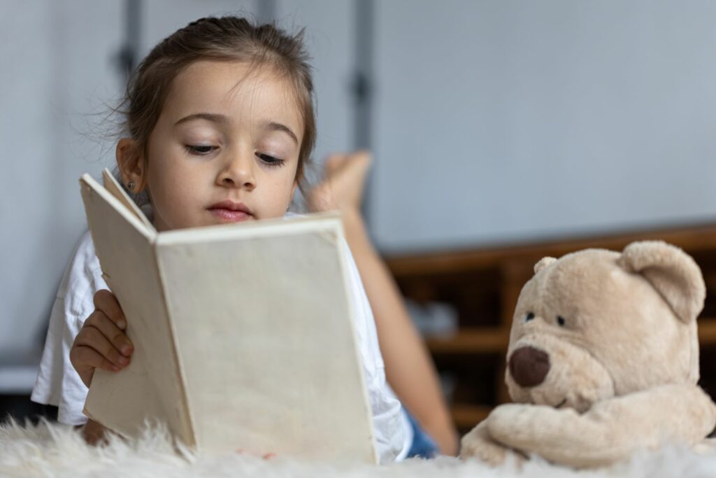 petite fille qui lie un livre accompagnée de sa peluche